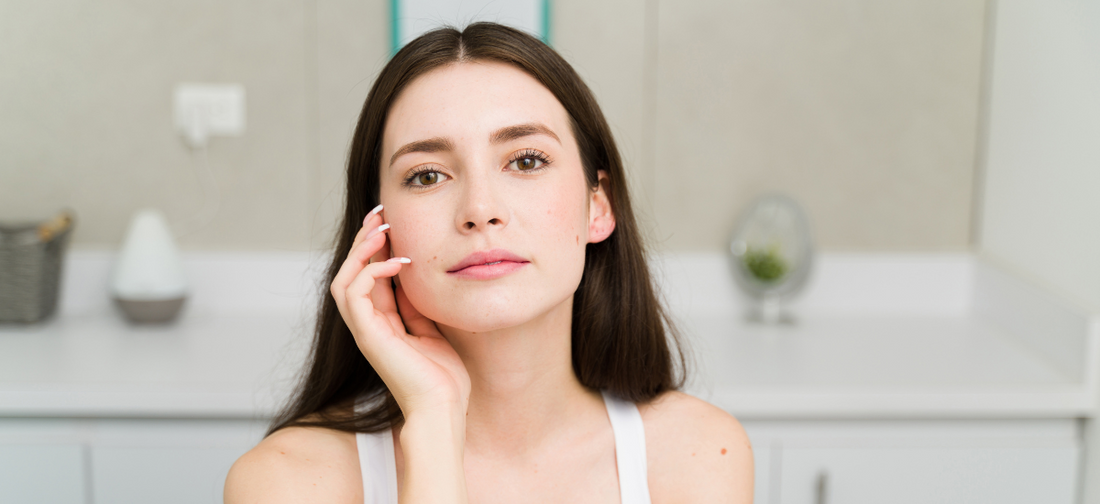 Mujer joven de cabello castaño toca suavemente su rostro en un baño luminoso