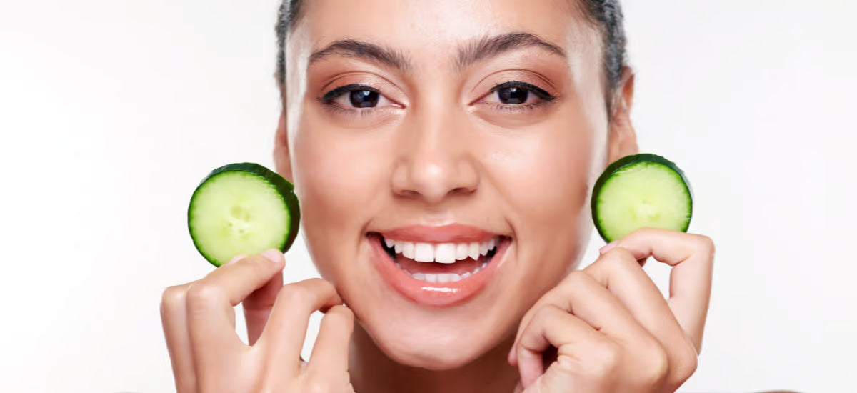La cara sonriente de una mujer que sostiene rodajas de pepino.