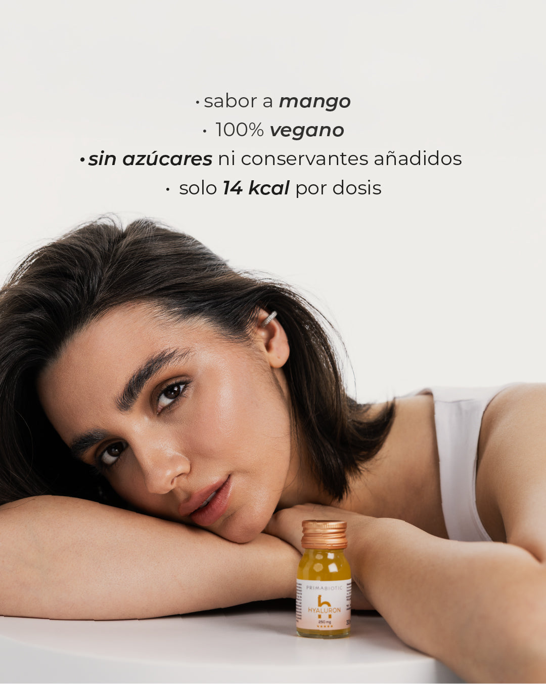 Mujer con botellita de ácido hialurónico Primabiotic, texto: sabor mango, vegano, sin azúcares, 14 kcal