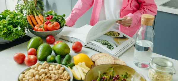 Persona revisando un libro de cocina con verduras frescas sobre la mesa, ideal para una dieta después de Navidad