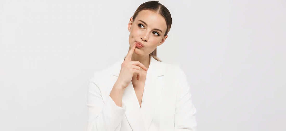 Una mujer elegante de cabello oscuro se plantea tomar suplementos de Collagen Primabiotic|Partículas de colágeno sobre fondo gris.