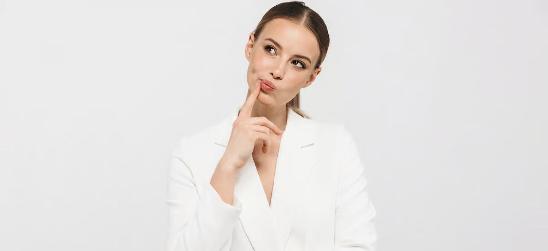 Una mujer elegante de cabello oscuro se plantea tomar suplementos de Collagen Primabiotic|Partículas de colágeno sobre fondo gris.