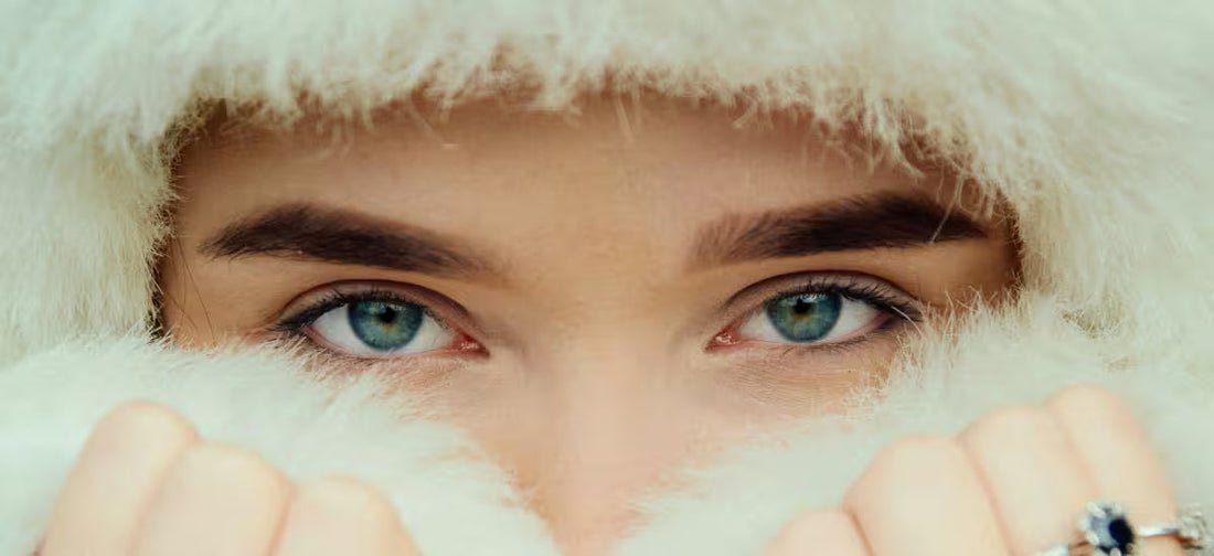 Primer plano de una mujer de ojos azules envuelta en un suave abrigo blanco, protegiendo su piel del frío invernal.