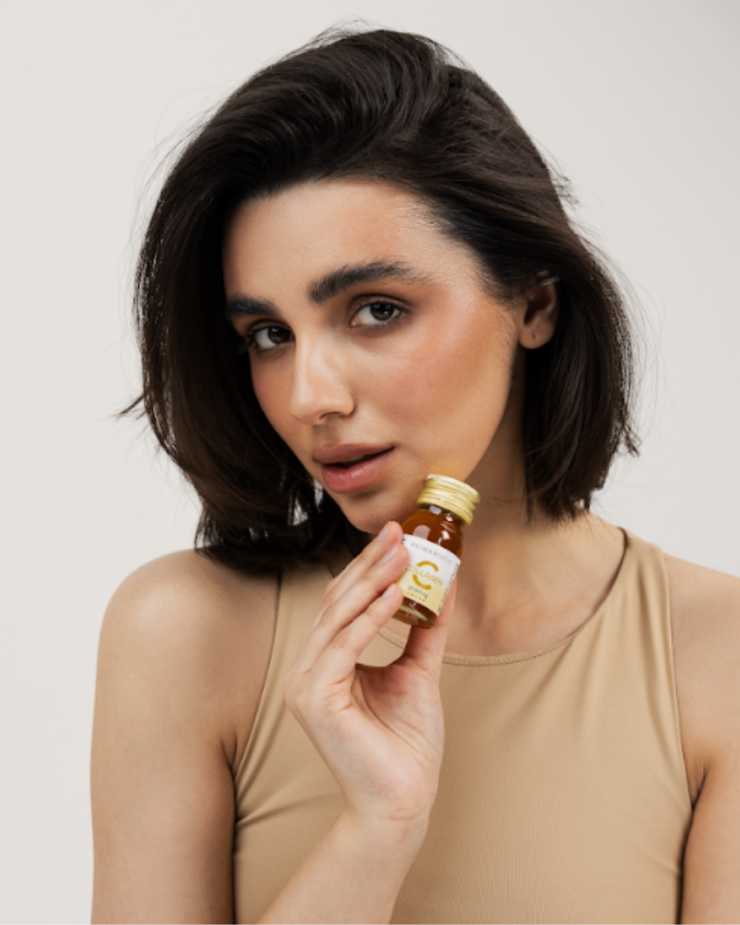 Mujer joven de cabello oscuro sostiene una botellita de suplemento de colágeno Primabiotic junto a su rostro