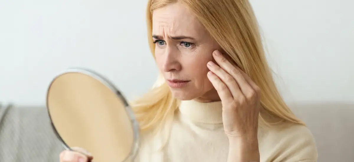 la mujer se mira la cara en el espejo y frunce el ceño